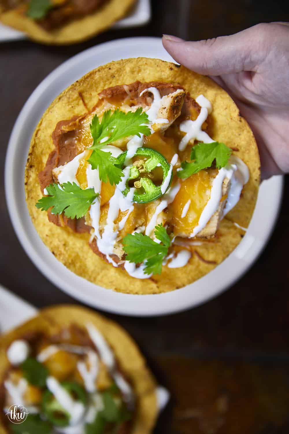 The crunch you've been craving! These Loaded Chicken and Bean Tostadas feature golden-baked shells, seasoned refried beans, juicy chicken, bubbly Mexican cheese, and spicy jalapeños. Finished with a cool sour cream sauce and fresh cilantro for that perfect creamy-meets-crunchy bite. If you love tacos, you have to try this 30-minute twist! #ChickenTostadas #30MinuteMeals #EasyMexicanRecipes #WeeknightDinnerIdeas #BudgetFriendlyCooking